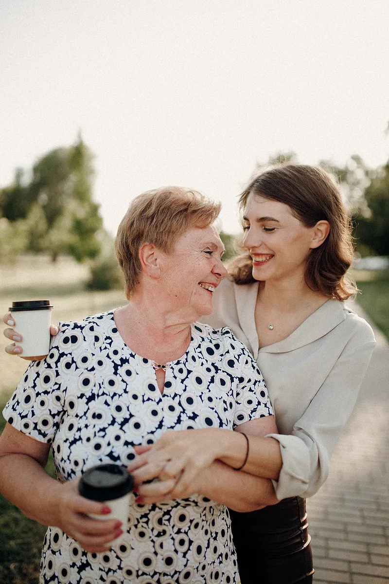 An older woman and a young woman share coffee in a park.