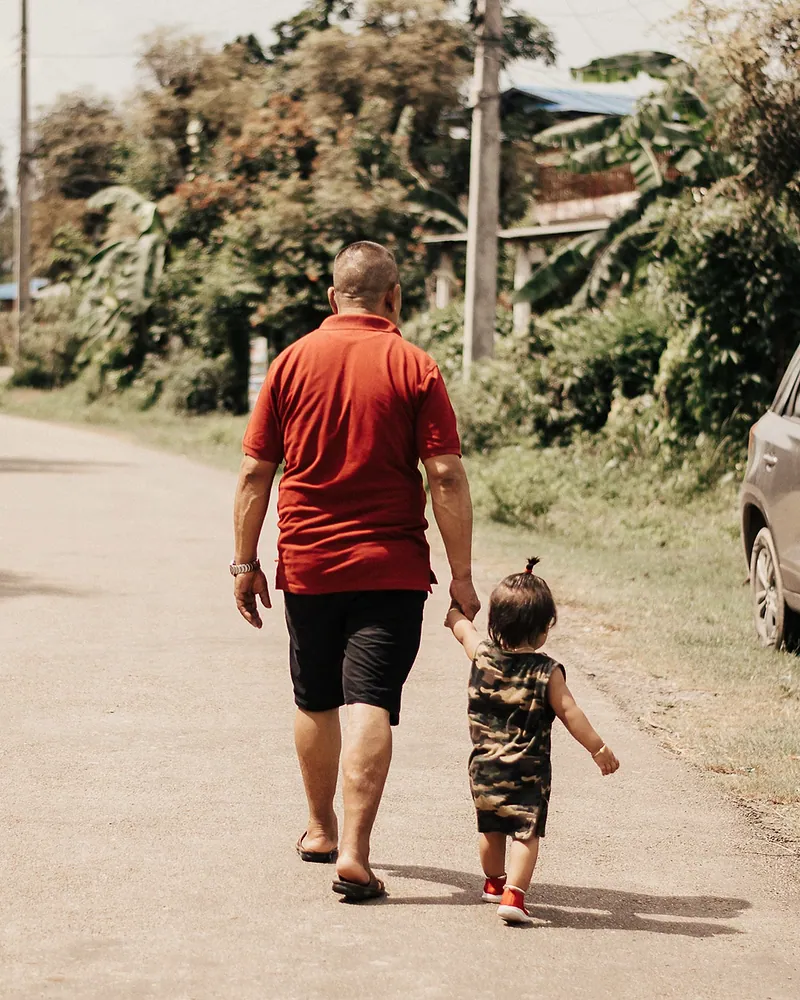 Un hombre camina de la mano de un niño pequeño por una calle rural.
